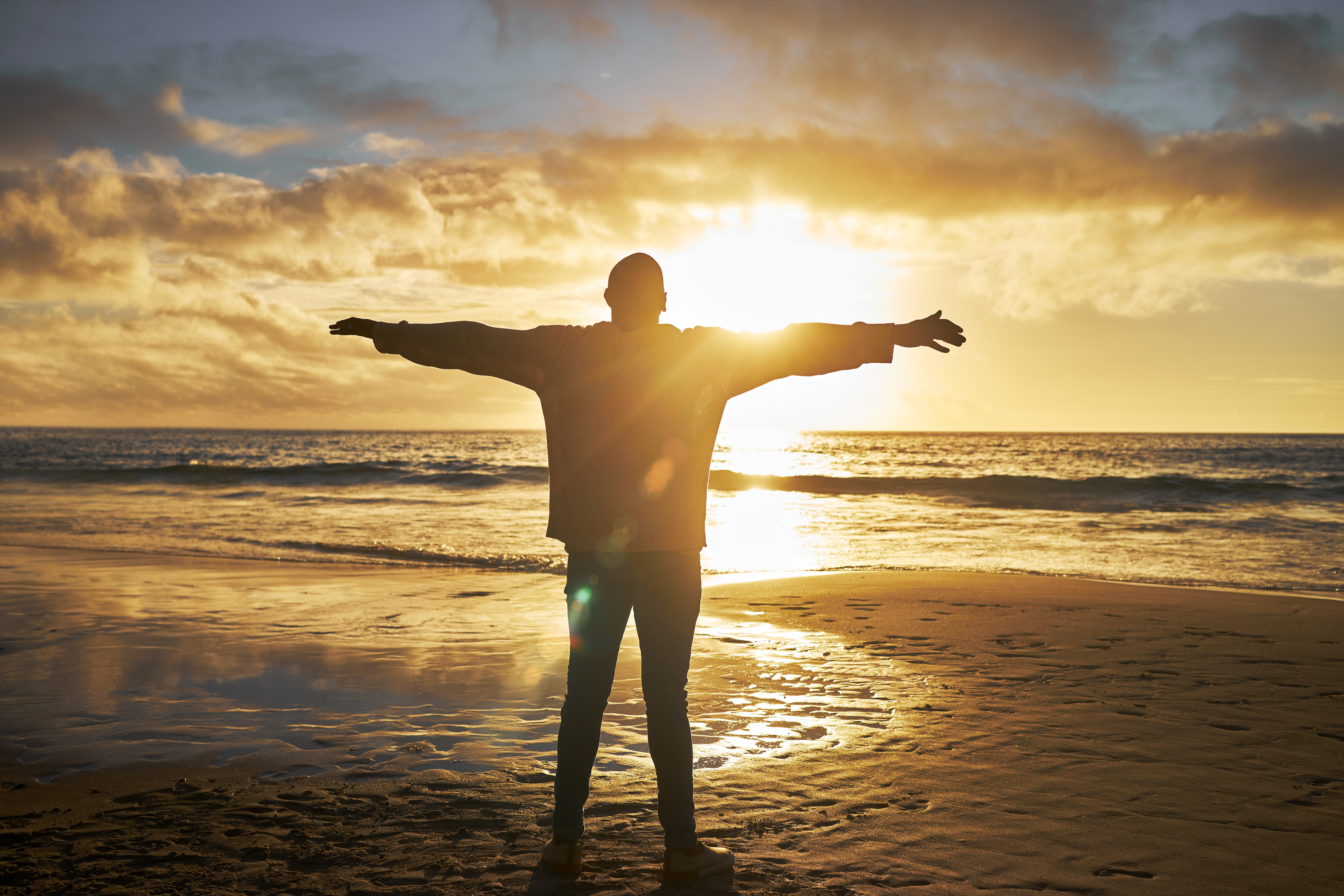 Worship, sunrise and silhouette of man at the beach standing with arms raised. Faith, religious and